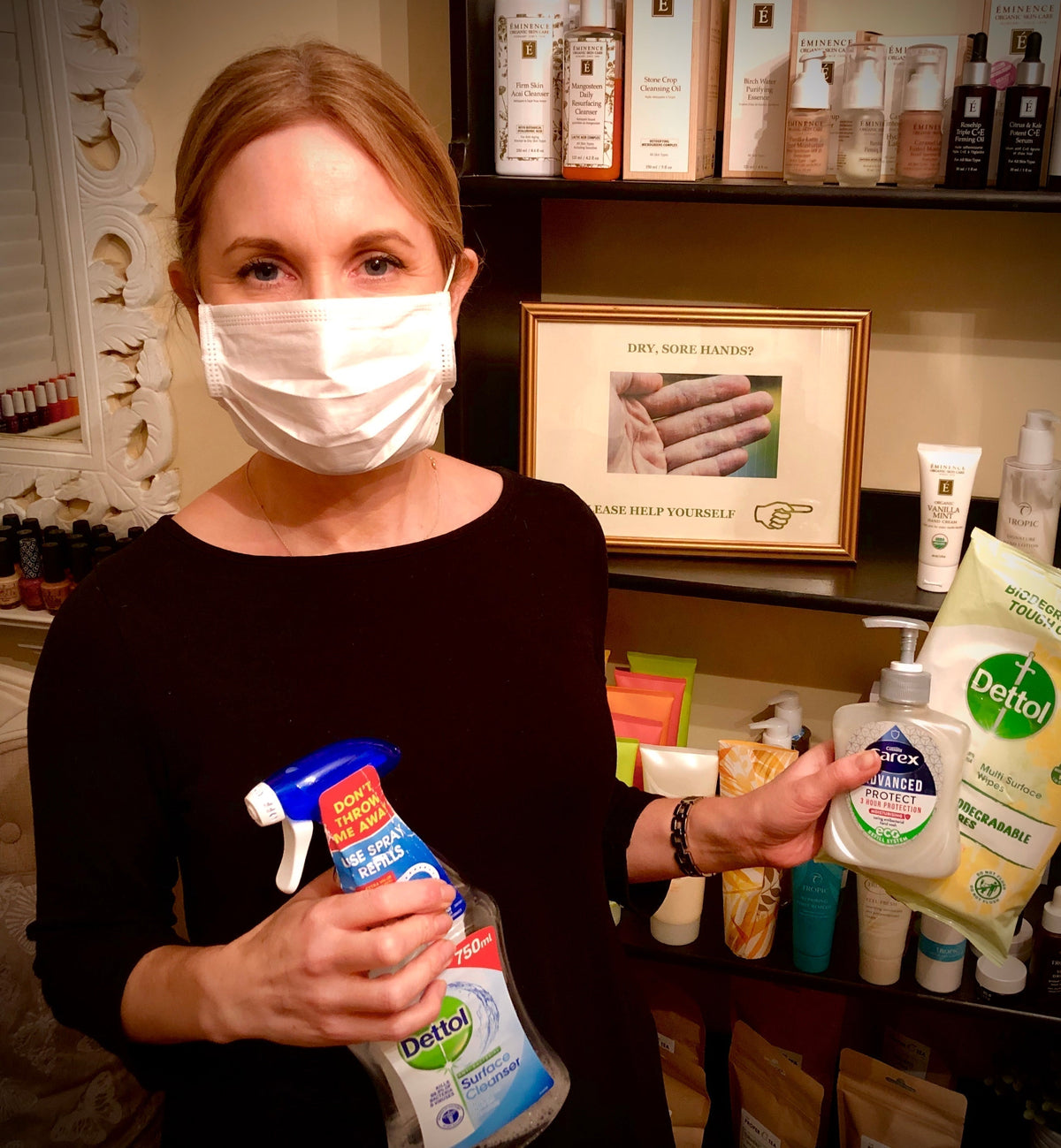 Karen wearing a face mask and holding cleaning spray and hand wash beside skincare shelves.