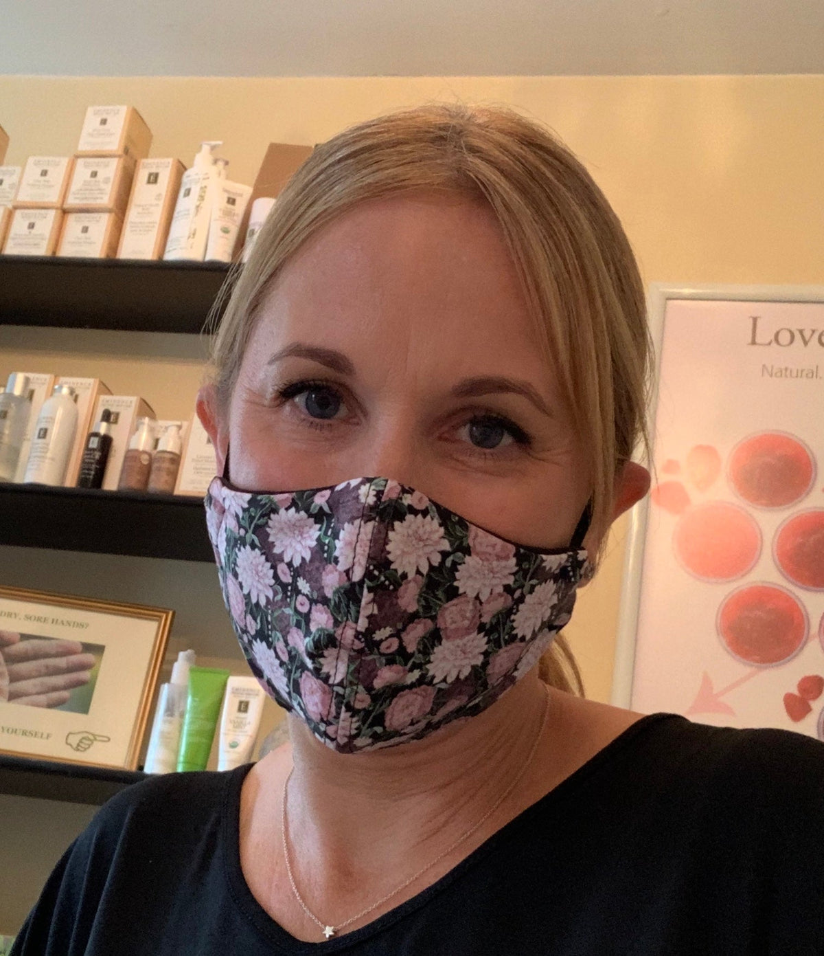 Karen wearing a floral face mask in her treatment space, with skincare shelves behind her.