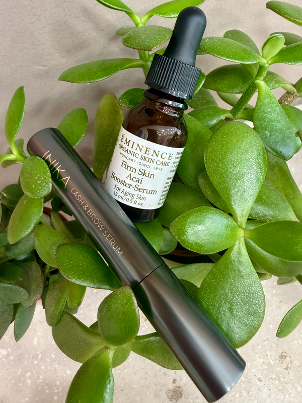 Two skincare products, a dropper bottle and a pen-style tube, on a light background with green leaves.