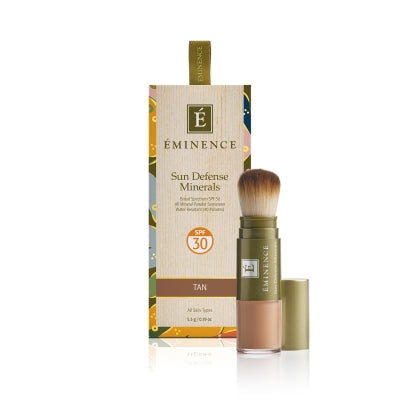 A box of Éminence Organic Sun Defense Minerals with SPF 30, showing the product name and the shade 'tan'. The product comes with a flow-through brush for application.