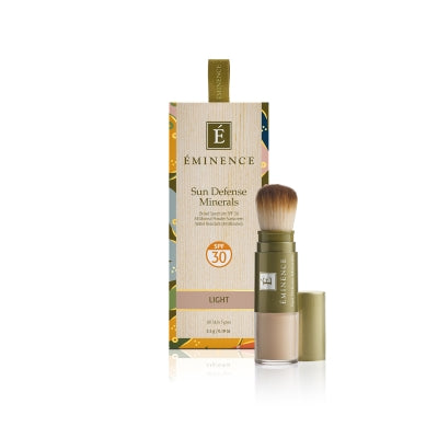 A box of Éminence Organic Sun Defense Minerals with SPF 30, showing the product name and the shade 'light'. The product comes with a flow-through brush for application.
