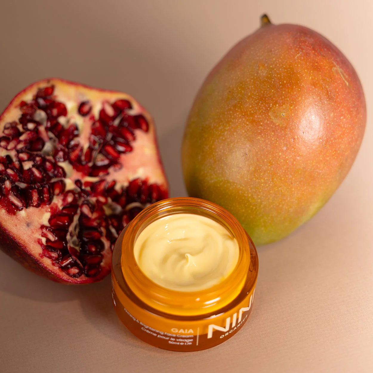 Jar of NINI Organic Gaia cream with a pomegranate and mango on a beige background