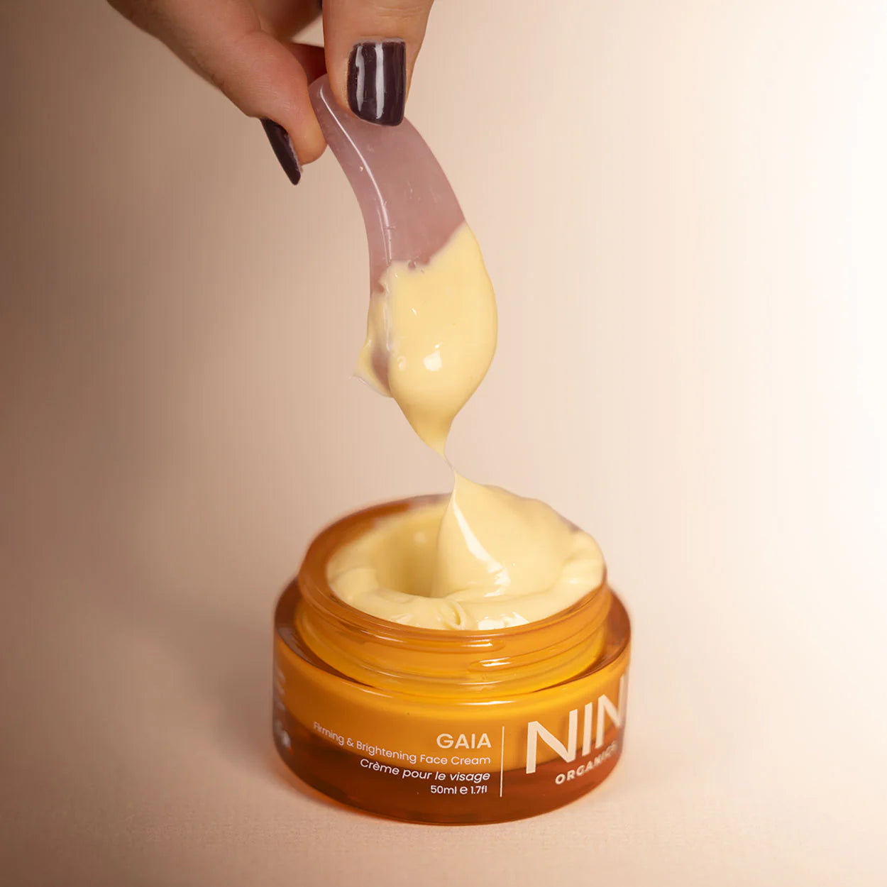 Nini Gaia face cream being scooped out with a spatula from a jar labeled 'GAIA'.