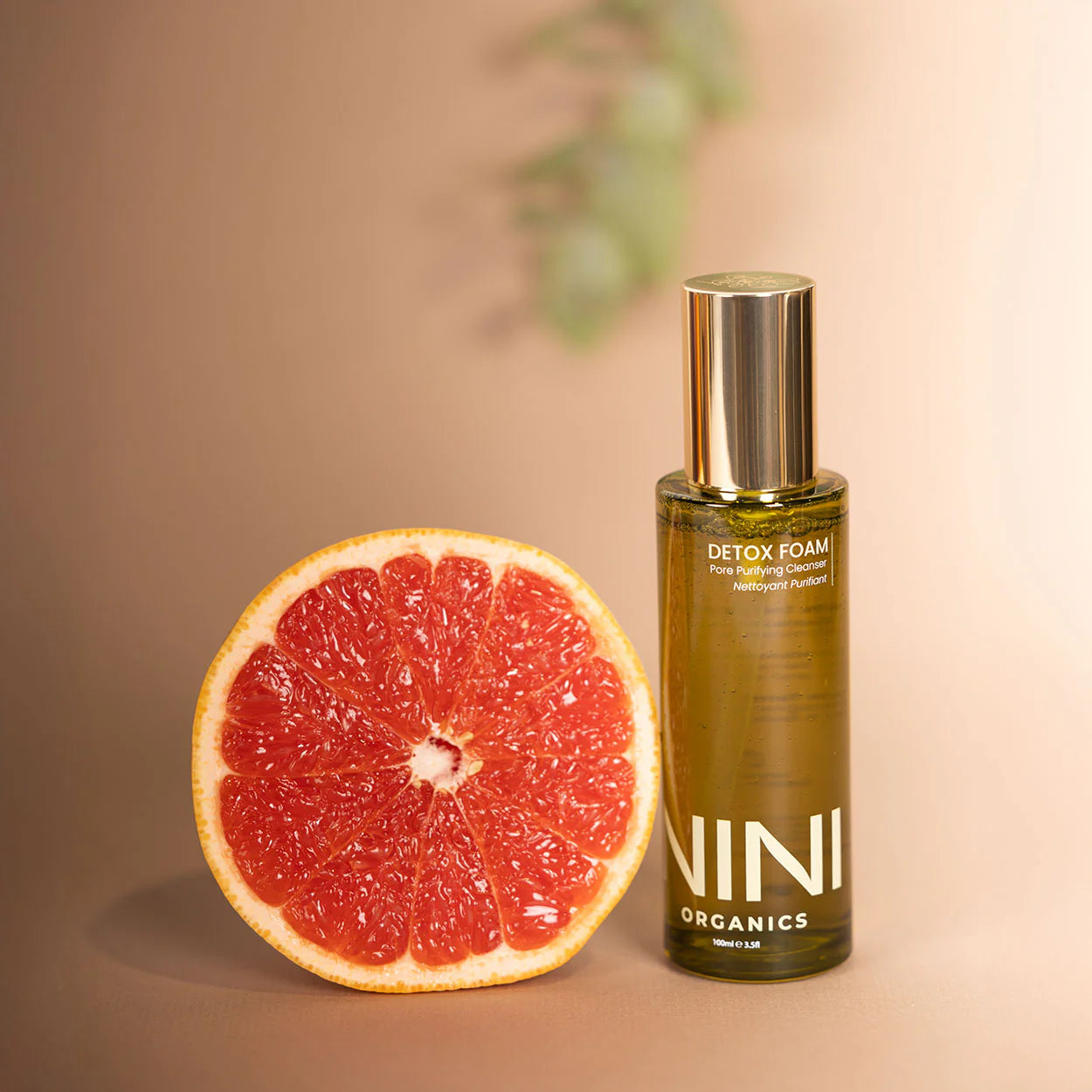 NINI Organics detox foam bottle next to a halved grapefruit on a beige background
