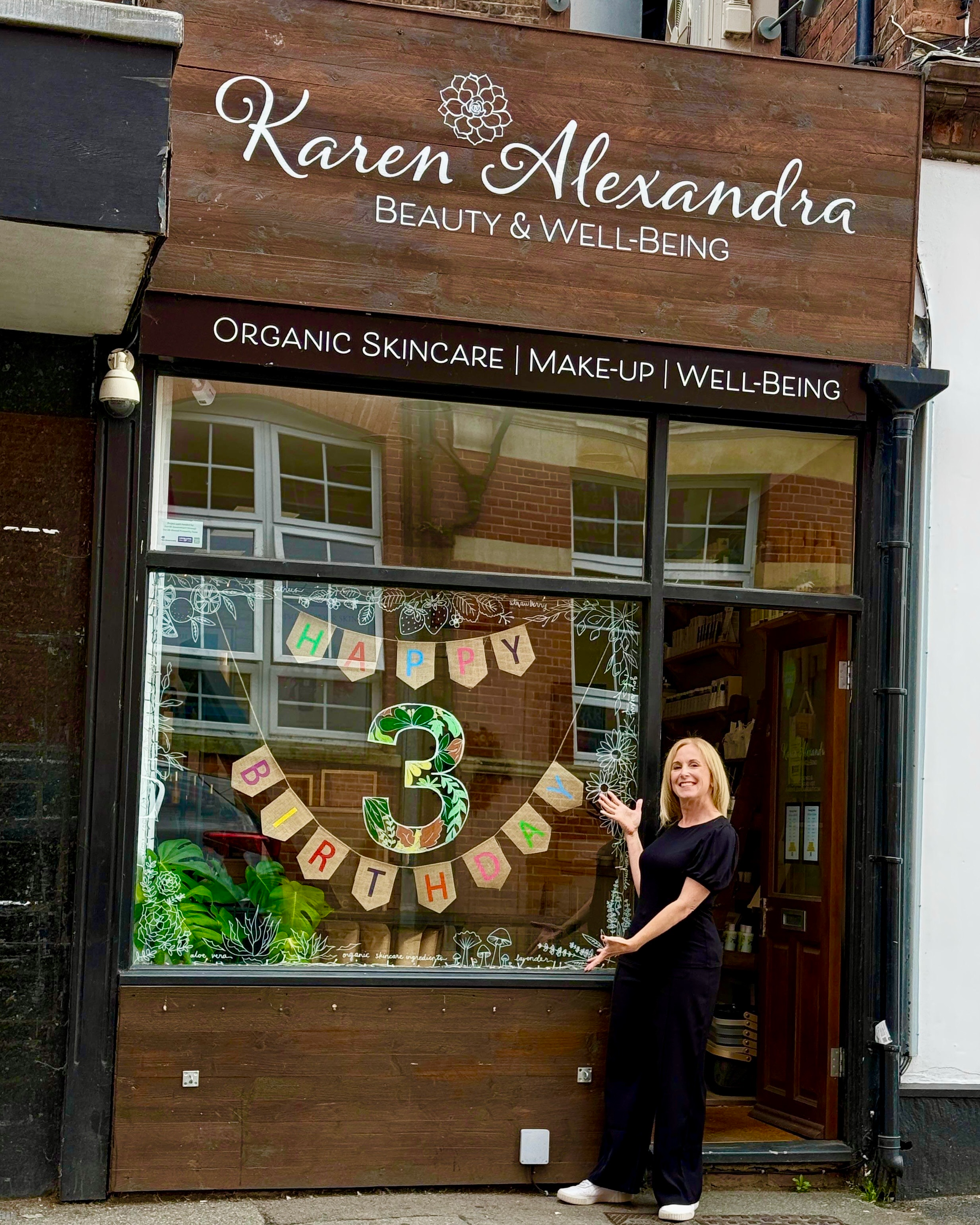 boutique shop window with owner standing outside celebrating 3rd birthday
