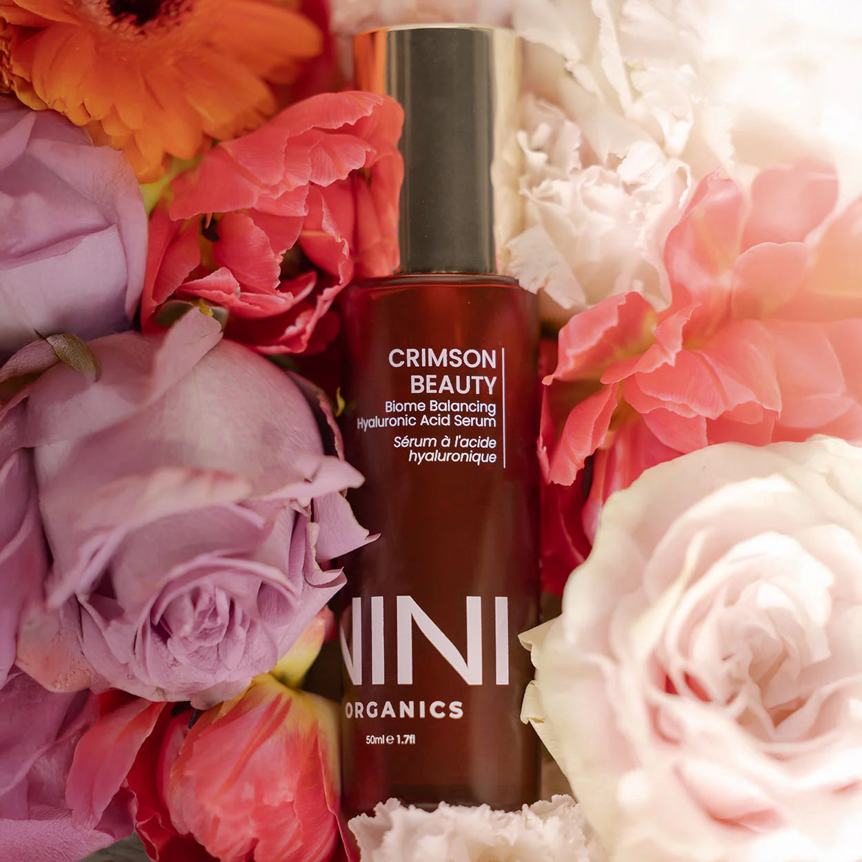 NINI Organic Crimson Beauty serum bottle surrounded by colourful flowers