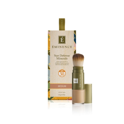 A box of Éminence Organic Sun Defense Minerals with SPF 30, showing the product name and the shade 'medium'. The product comes with a flow-through brush for application.
