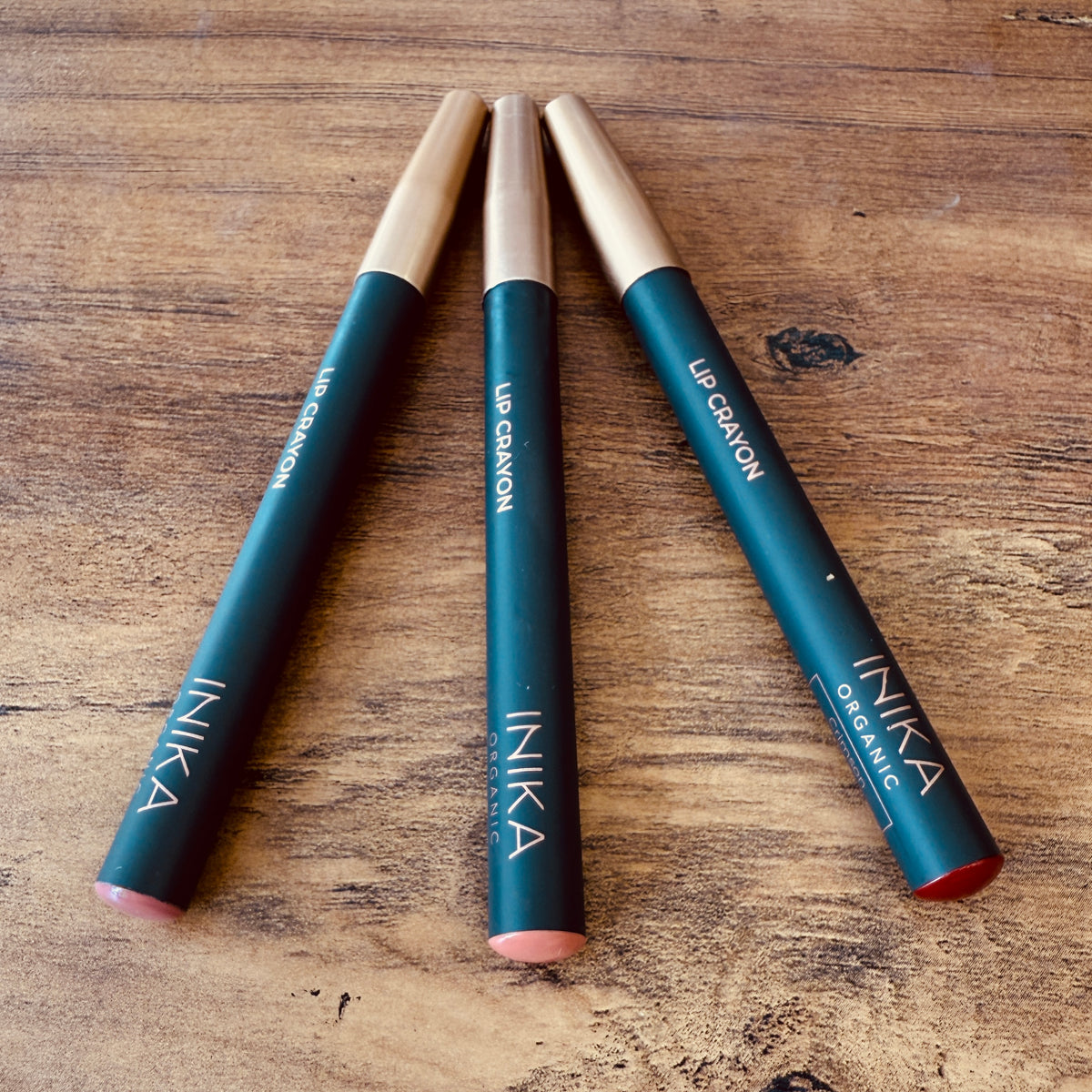 Three INIKA lip crayons on a wooden surface