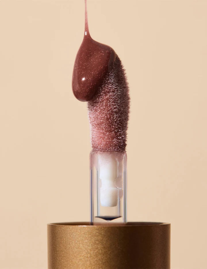 Close-up of a brown nail polish bottle with a brush on a beige background