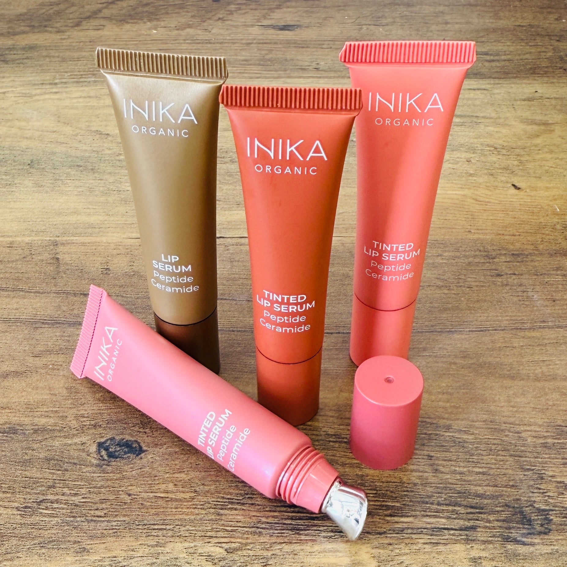 Set of INIKA organic lip serum tubes on a wooden surface