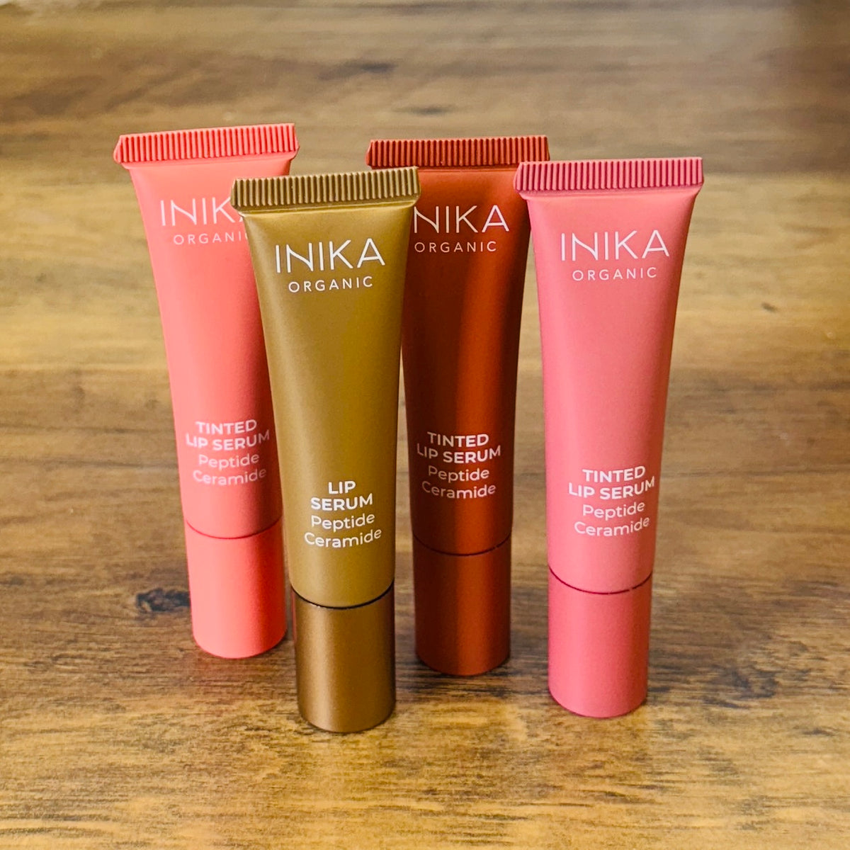 Four INIKA lip serum tubes on a wooden surface