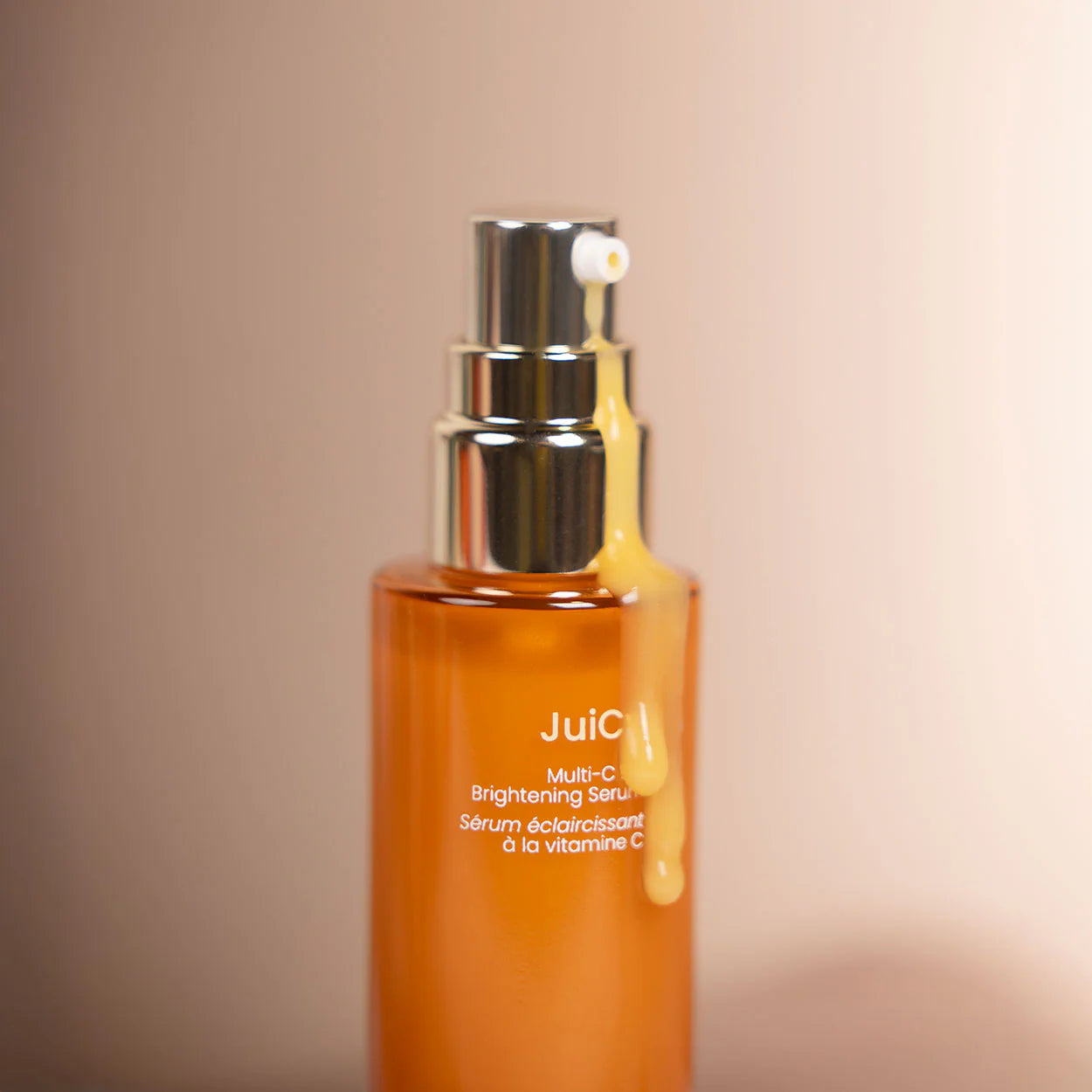 NINI Organics Juicy Vitamin C serum bottle with silver pump on a beige background
