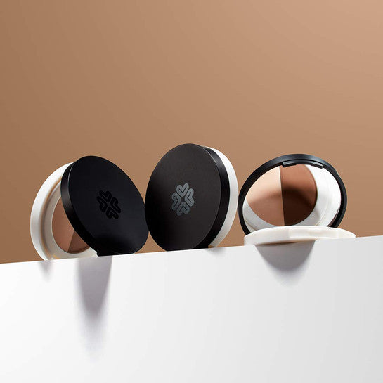 Lily Lolo Eye Brow Duo product with pressed powder and wax in a sleek black and white compact, displayed on a white surface with a beige background.