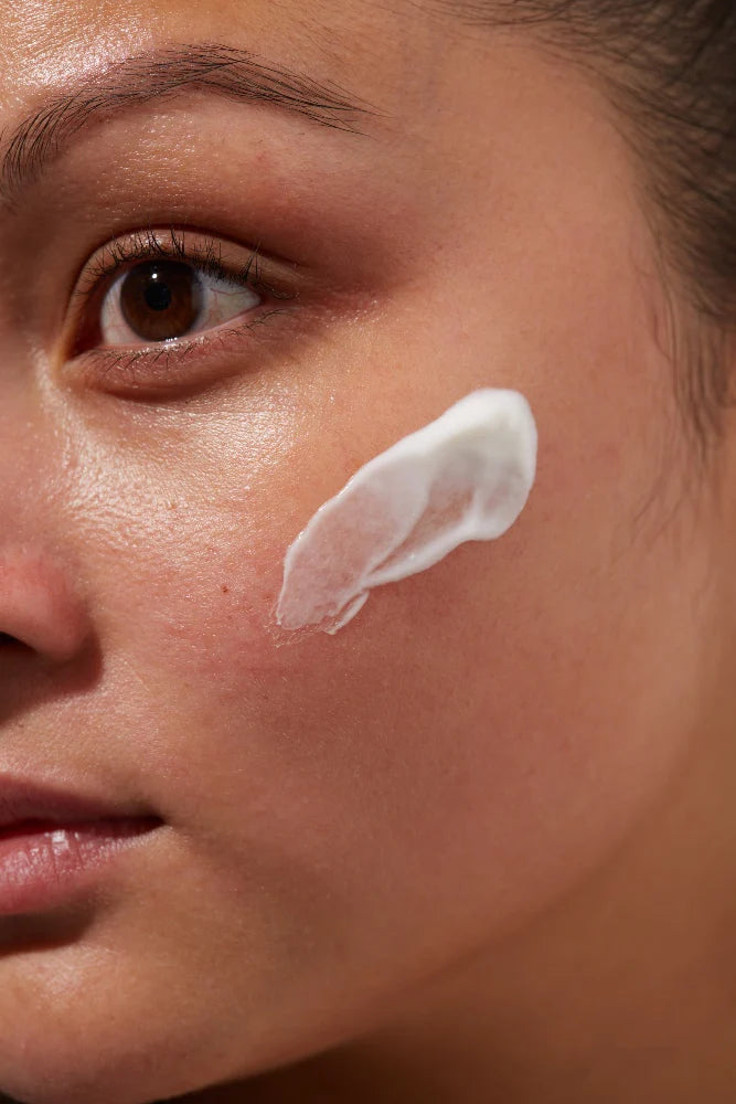 Close-up of a models face with a small amount of NINI Organics Oatopia cream cleanser on their cheek.