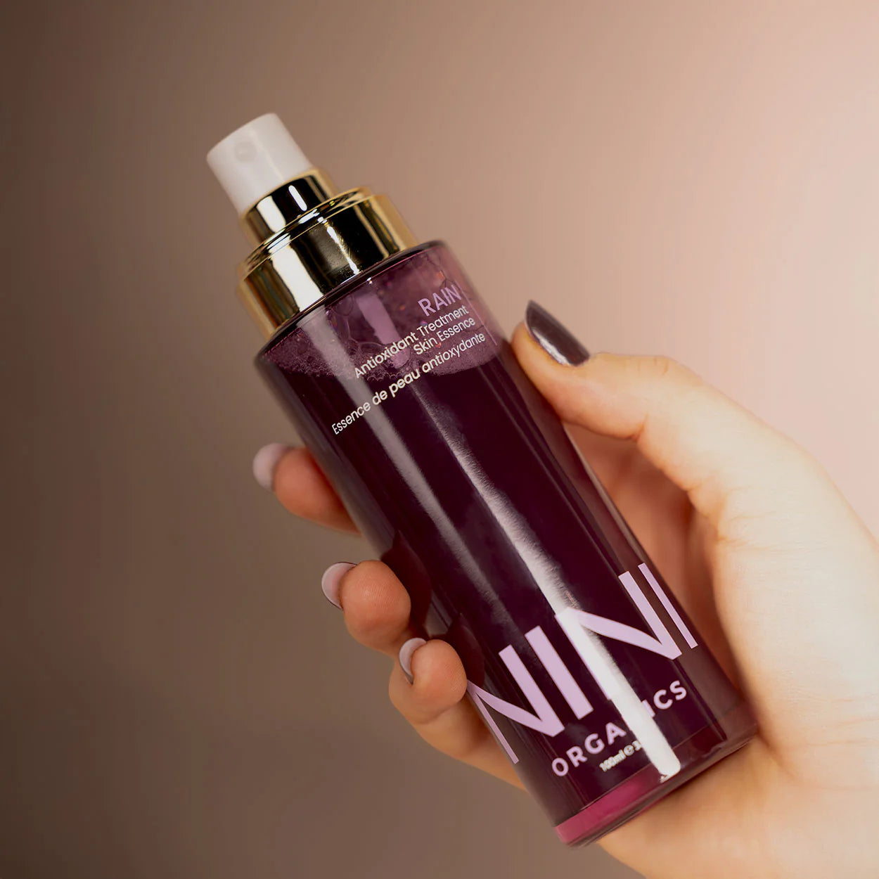 Hand holding a NINI organics Rain face mist skincare bottle against a neutral background
