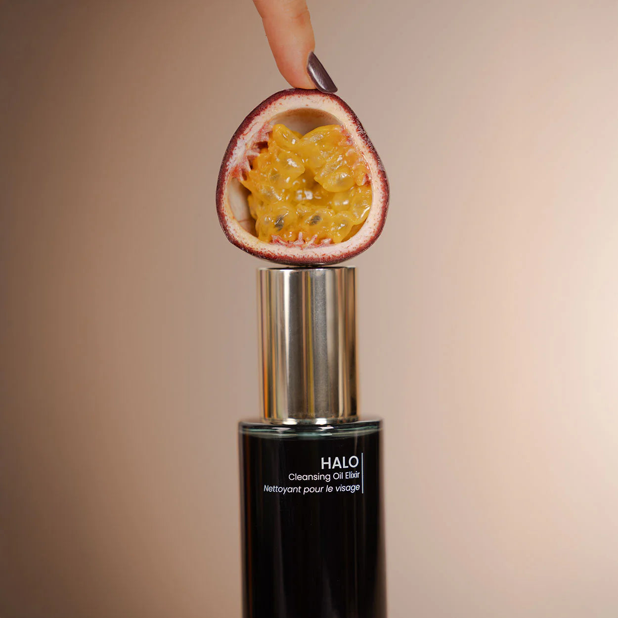 HALO cleansing oil bottle with a halved passion fruit on a beige background